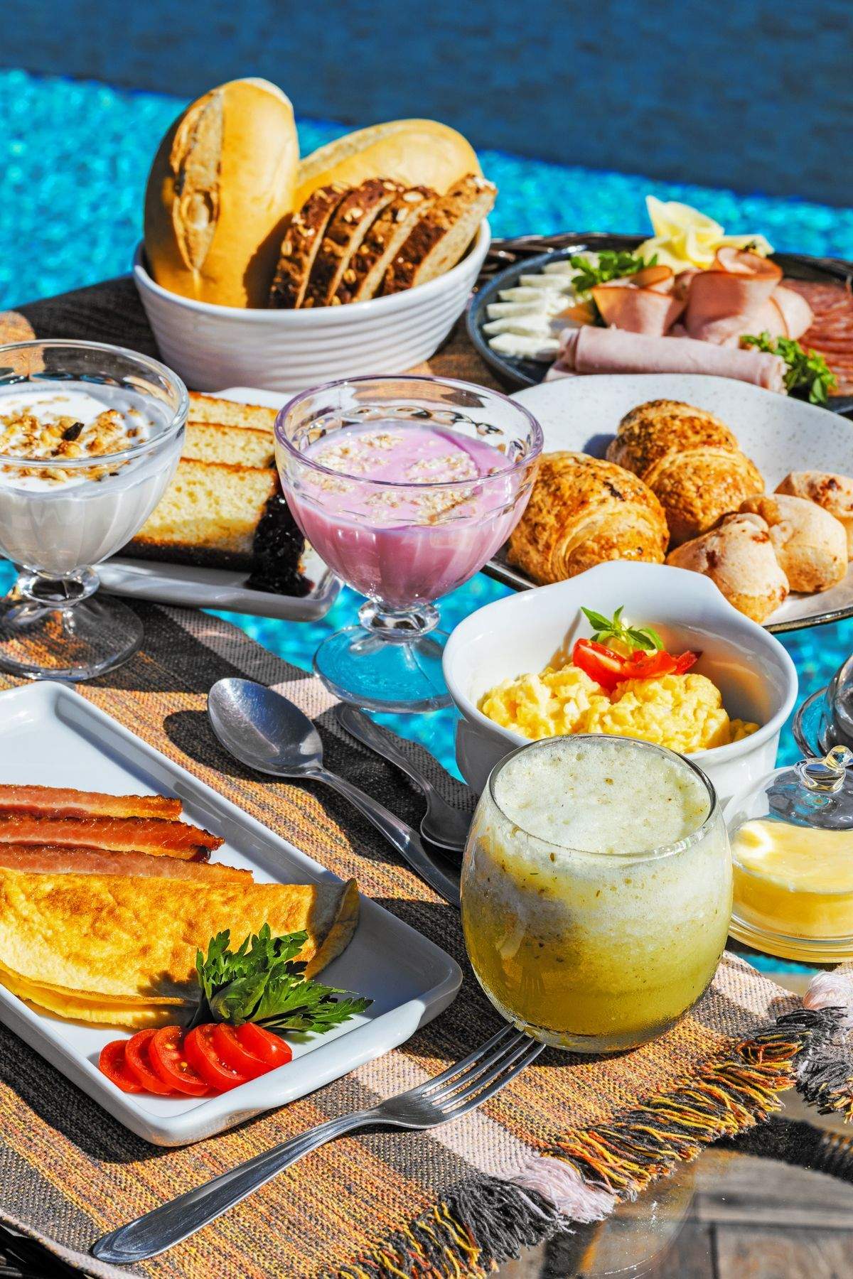 Uma mesa com pratos de comida e bebidas ao lado de uma piscina.